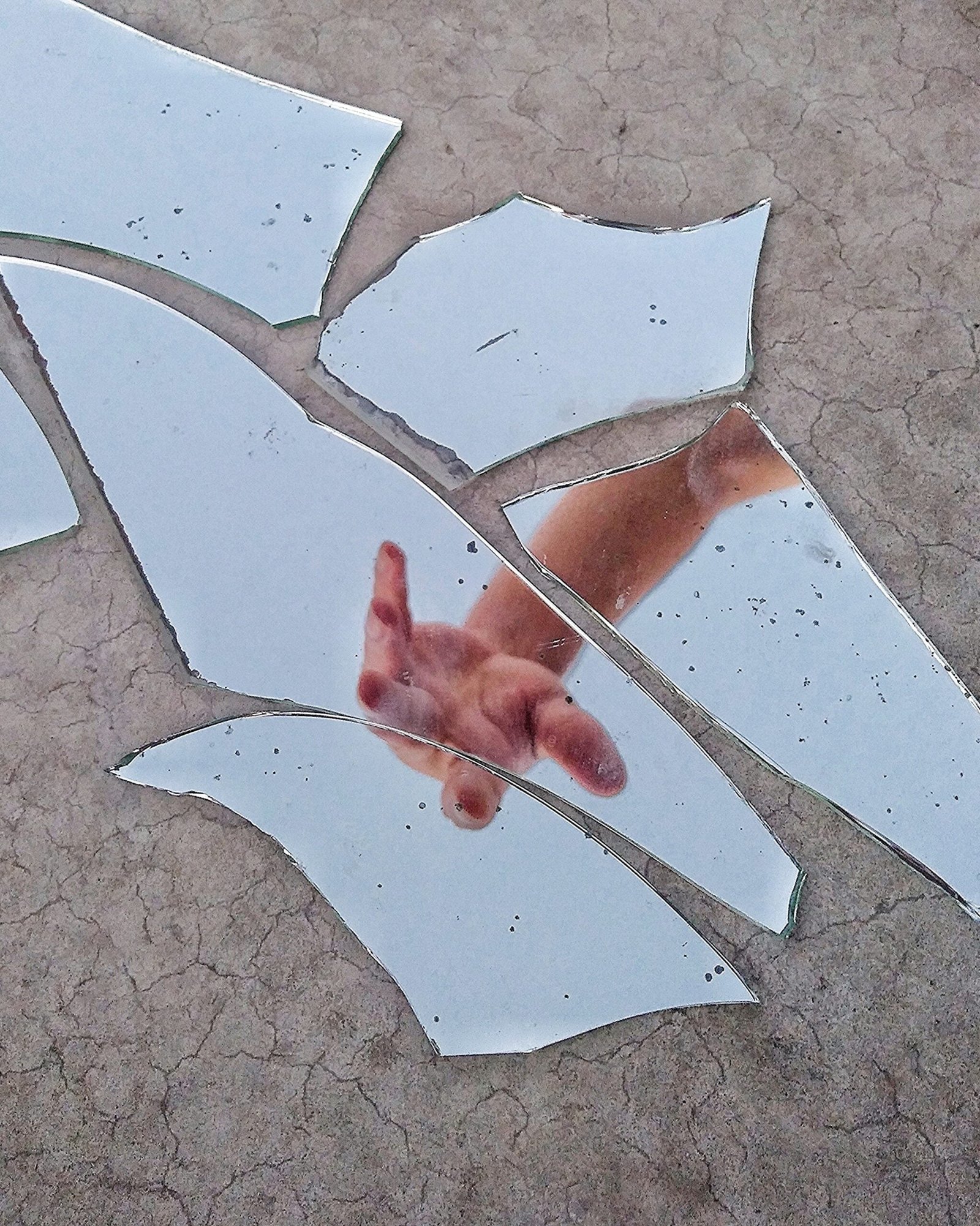 A photograph of a broken mirror reflecting a hand