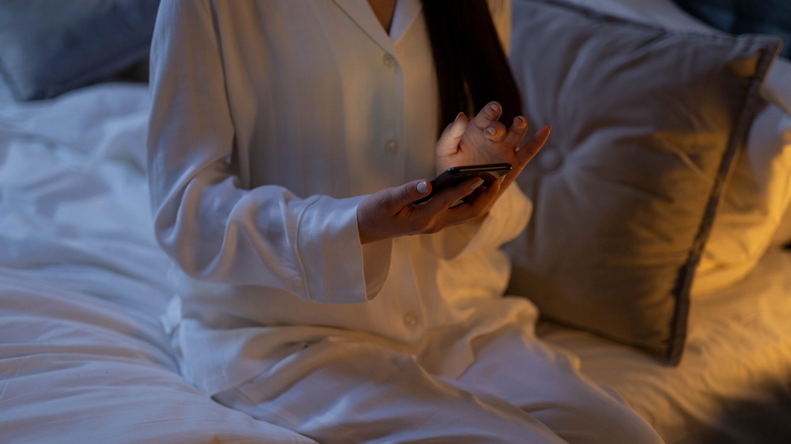 A woman using her phone in bed which is bad for sleep due to the light emitted